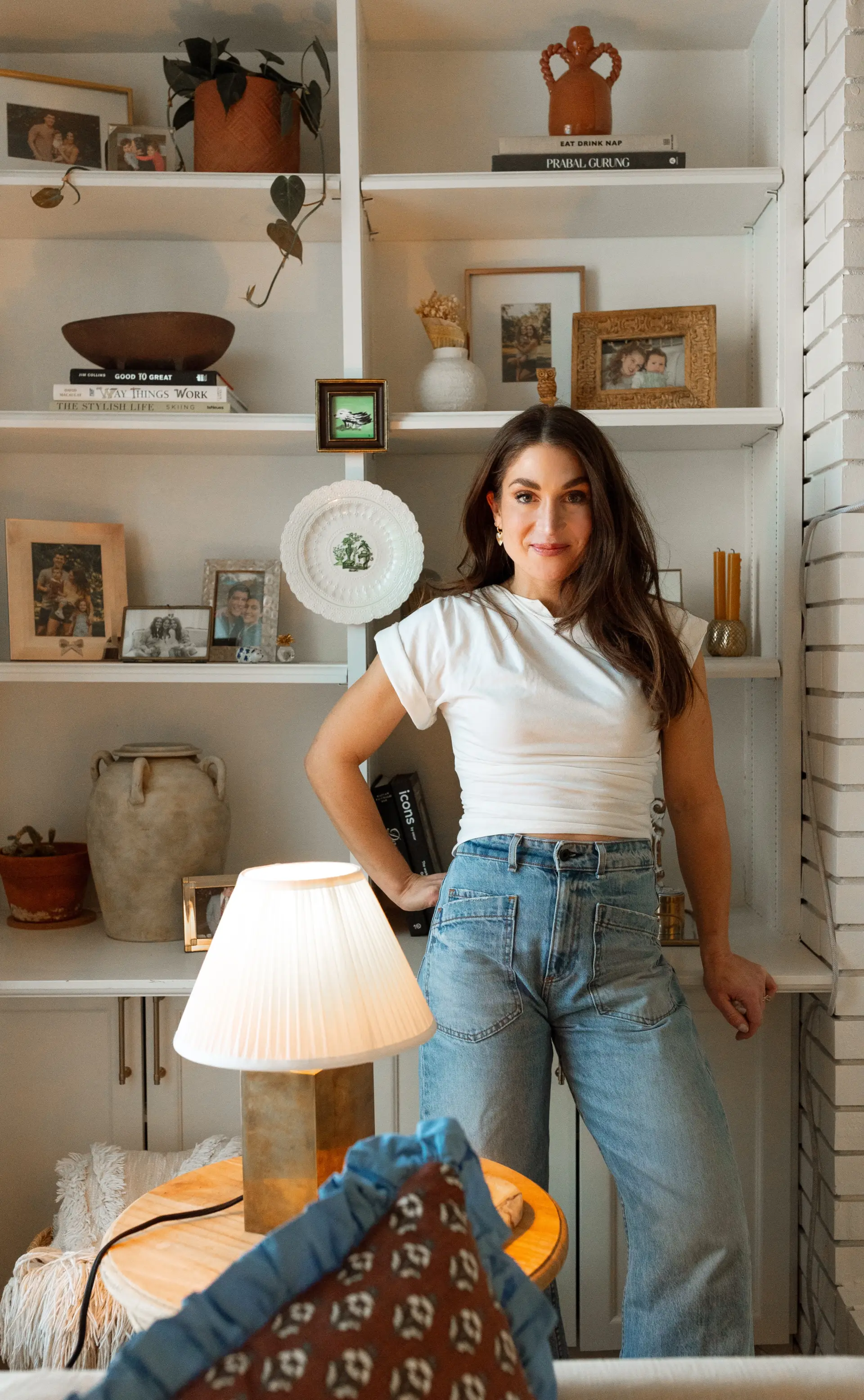 Katherine Hagen standing beside styled bookshelves and a table lamp